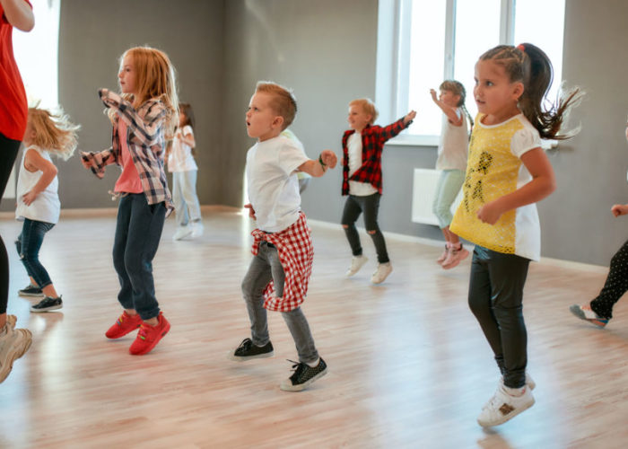 Full of energy. Group of little boys and girls dancing while having choreography class in the dance studio. Female dance teacher and children